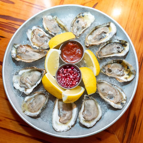 A dozen fresh oysters on the half shell with lemon wedges, cocktail sauce, and mignonette on ice.