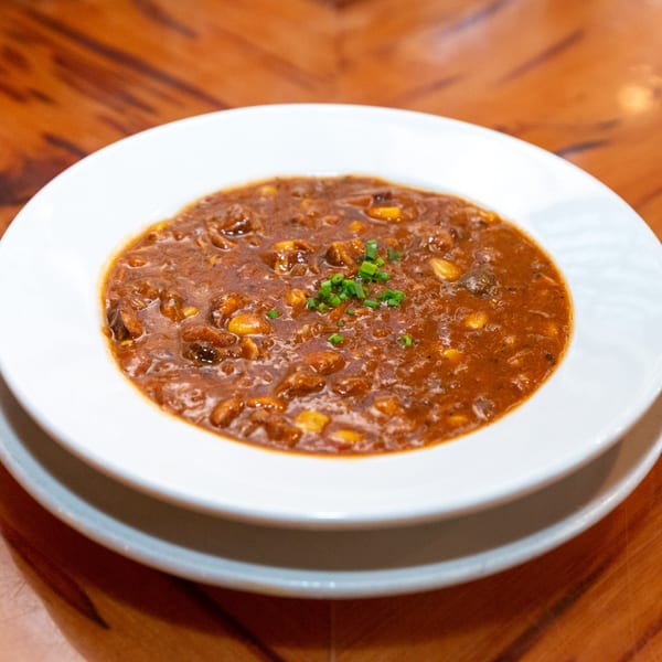 A bowl of Big Daddy's NY BBQ chili, garnished with chopped green onions, on a wooden table.